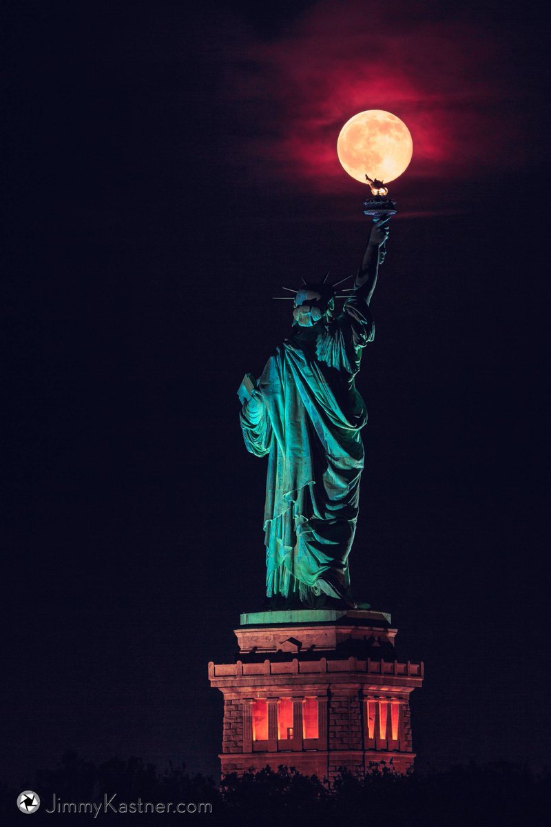 Superbe photo d'une pleine lune en équilibre sur la torche de la Statue de la Liberté de NY