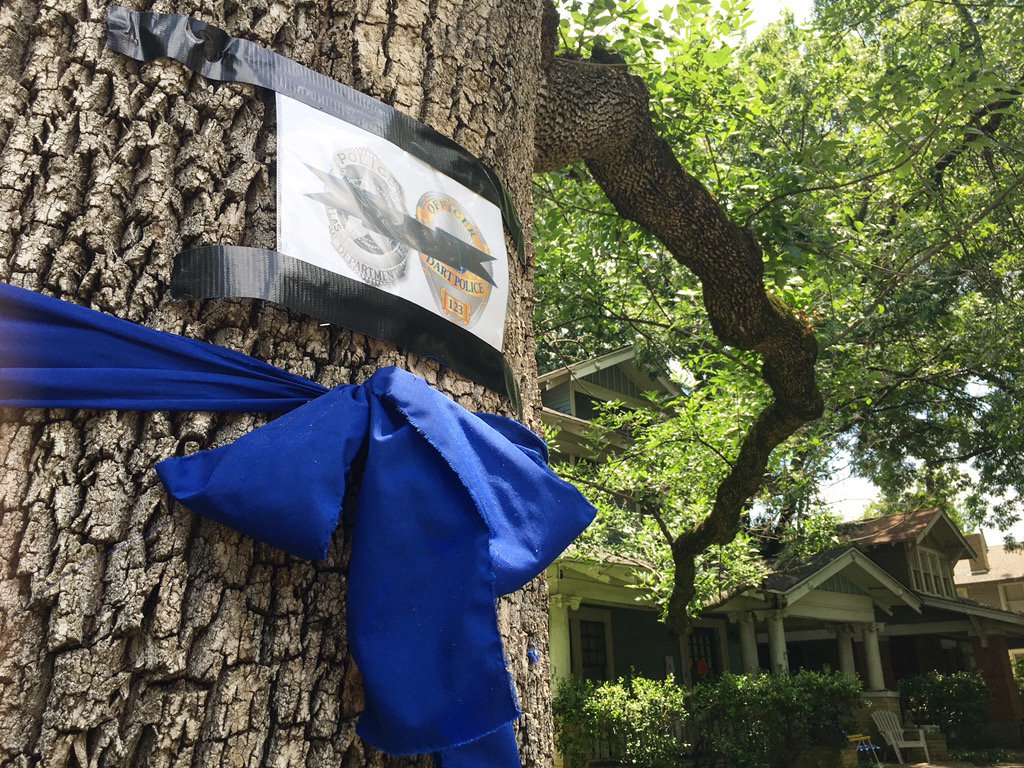 wfaa's tweet photo. Trees on Bryant St. in Dallas have been wrapped w/blue ribbons, markers to honor our fallen officers. #StandUnited https://t.co/n8SnP3CjvT