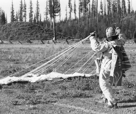 A smokejumper gathers his chute after landing near Seeley Lake, Montana in 1940.