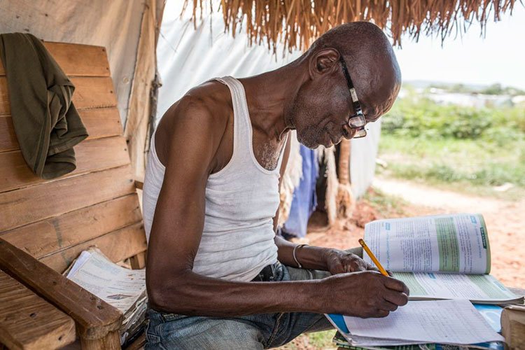 ICRC's tweet image. 71-year-old Alfred is a teacher in Bangui, #CAR. He prepares lessons for local kids by his tent at a displaced camp.