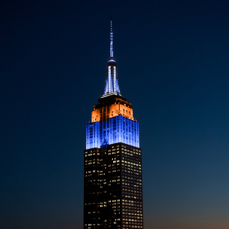EmpireStateBldg's tweet image. Our lights glow in orange and blue as we wish the @Mets good luck against the @SFGiants in the @MLB #NLWC game tonight. #LetsGoMets