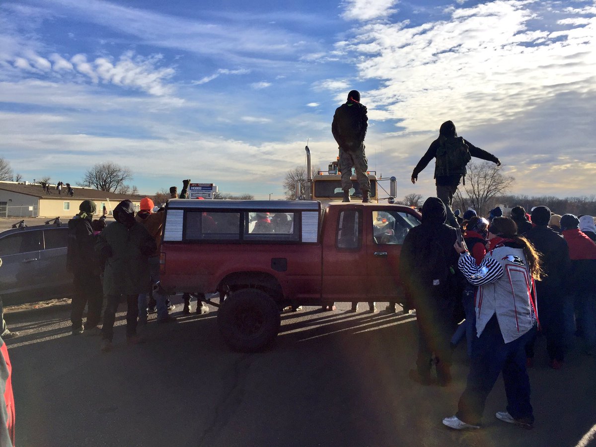 KWRose's tweet photo. Water protectors rush to train tracks to slow down work on the pipeline. Police run in to keep them back. Cars still blocking road. #NoDAPL https://t.co/Aa5Nq25I68