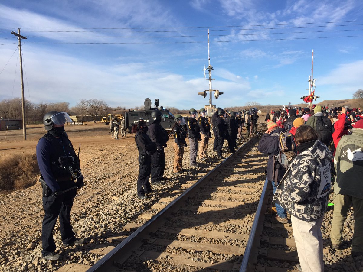 KWRose's tweet photo. Water protectors rush to train tracks to slow down work on the pipeline. Police run in to keep them back. Cars still blocking road. #NoDAPL https://t.co/Aa5Nq25I68