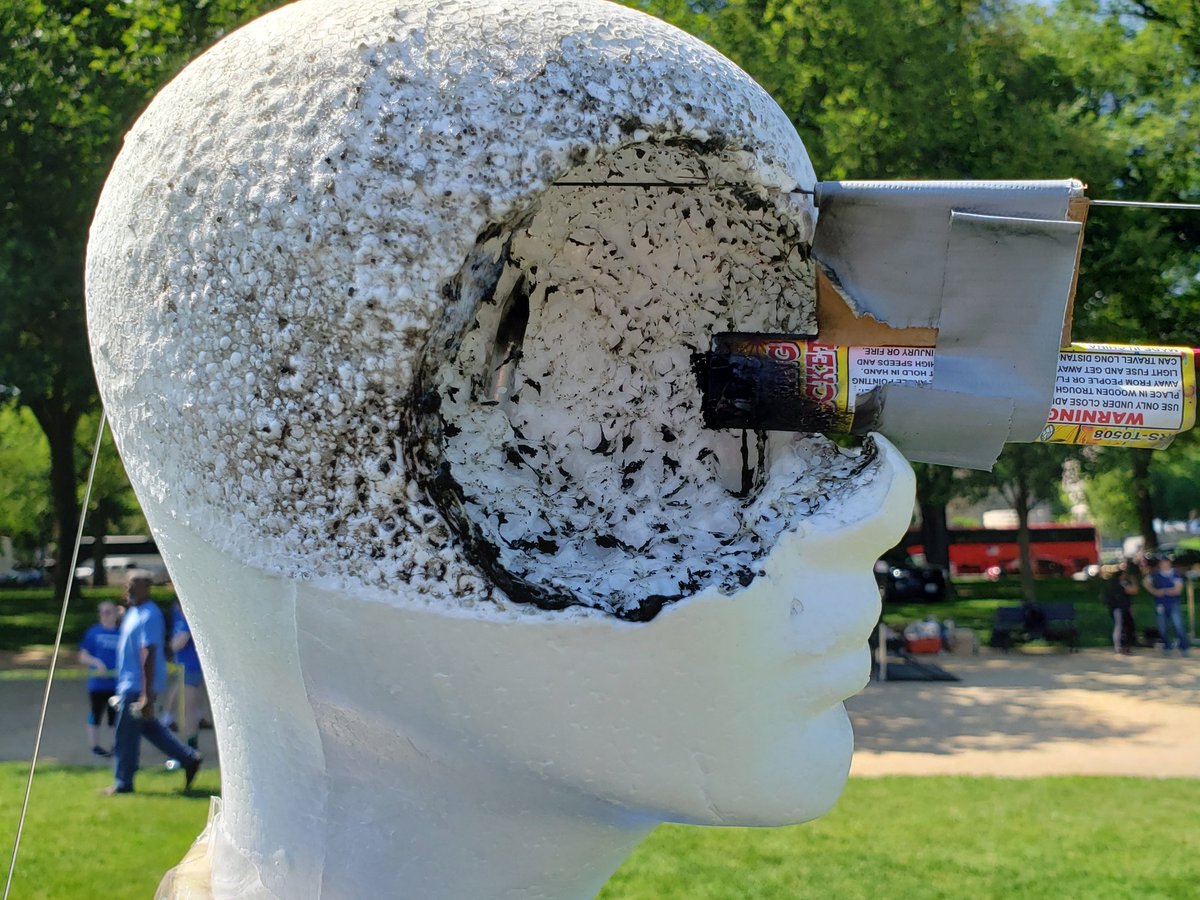 A photo of a fake head with a bottle rocket sticking out of its eye.