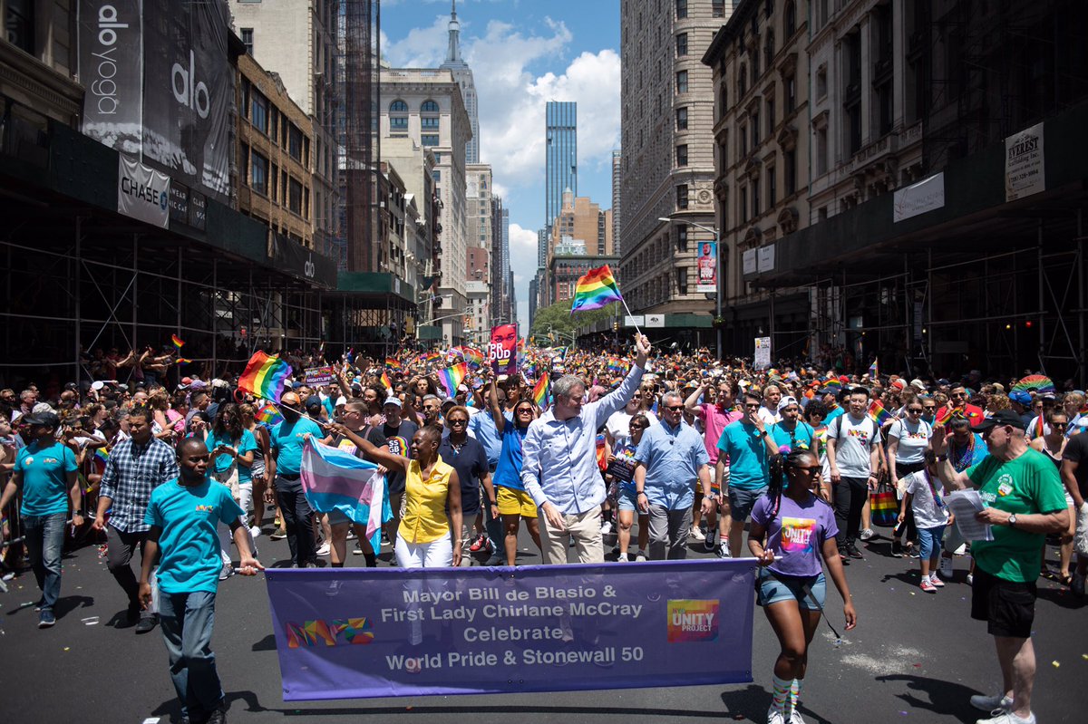Mayor walking holding rainbow flag with large crowd in front of sign with his name on it