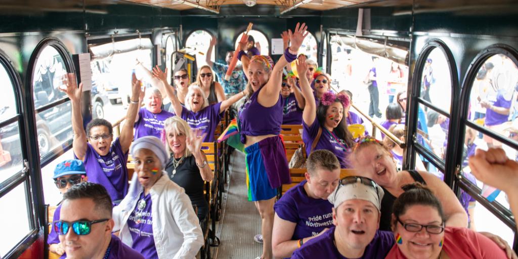 A group of Northwestern Medicine and Northwestern University employees and physicians smile wide and raise their hands on the trolley ride to the 50th Chicago Pride Parade.