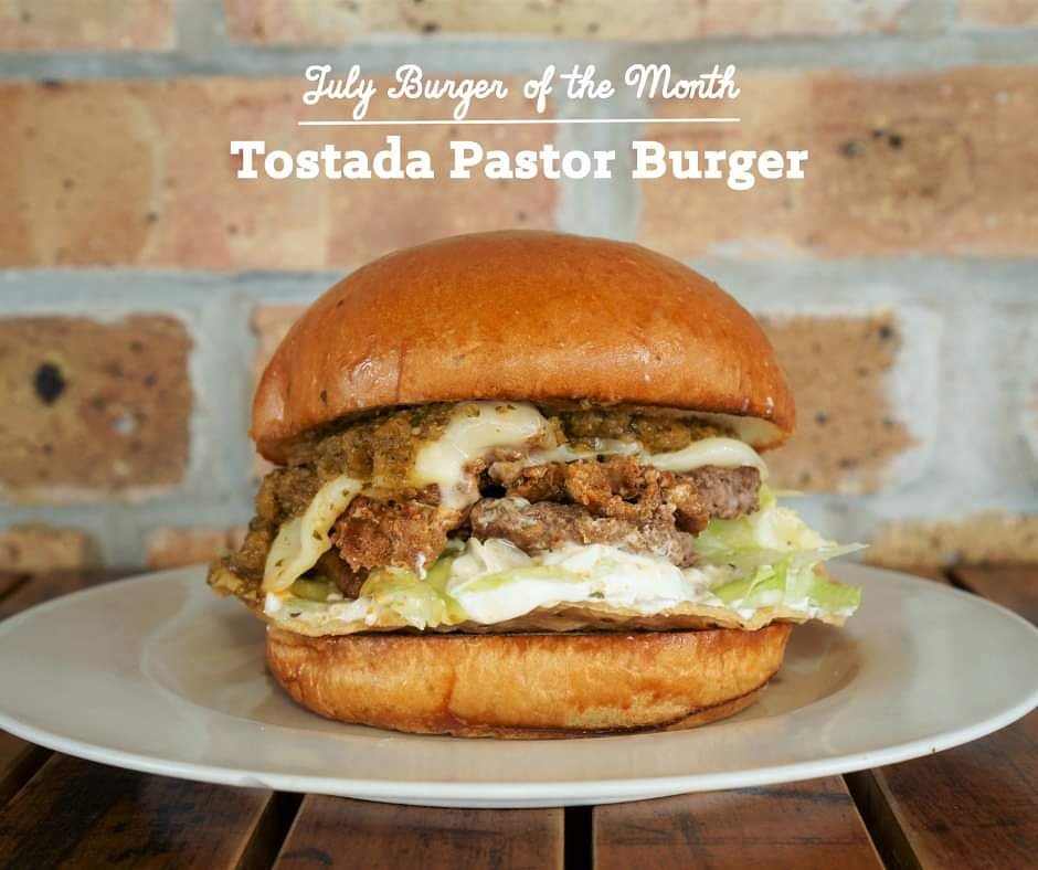 New month; new tasty burger special! Stop in anytime this July and try our traditional recipe Tostada Pastor Burger!

Our signature burger topped with in-house marinated pastor pork, from-scratch salsa verde, crispy tostada, lettuce, sour cream &amp; provolone on your choice of bun.