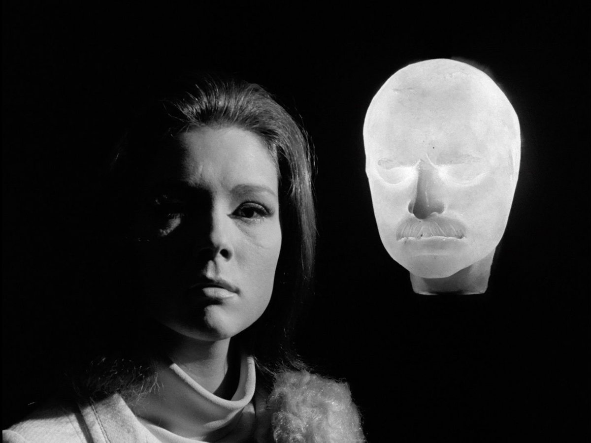 Mrs Peel in the dark with Keller’s glowing mask behind her