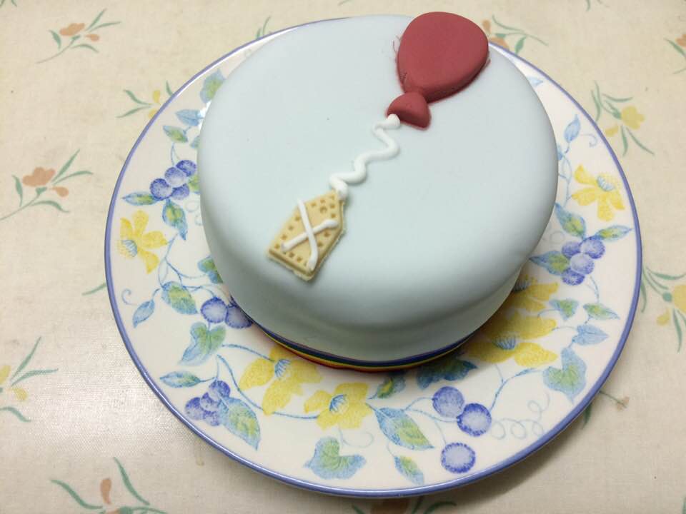 A small but perfectly formed birthday cake with icing and what looks like a balloon.