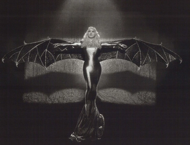 Mae West in a shiny, slinky dress with dramatic bat wings