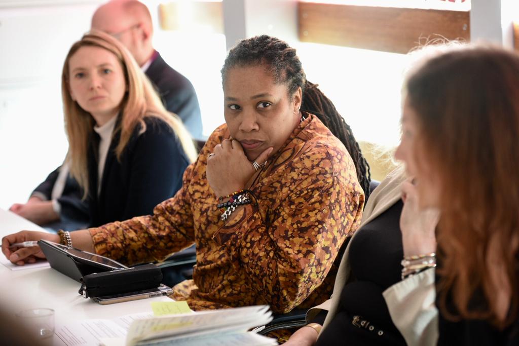 Four people, three women and one man, sit on one side of the conference room table, listening with thoughtful expressions.
