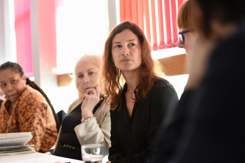 Four women sit on one side of the conference room table, listening with thoughtful expressions.