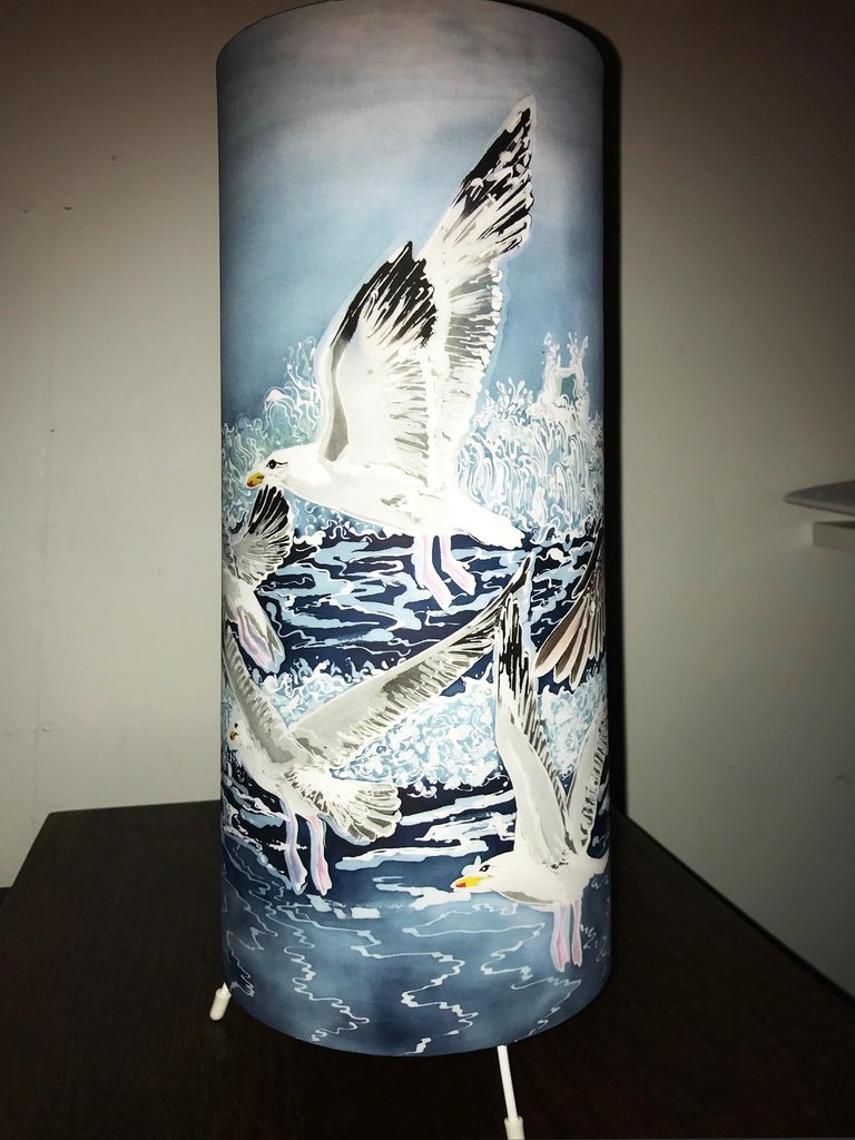 king_therese's tweet photo. Here is another of my batik painting designs that has been transferred to another product - an elegant cylindrical table lamp featuring a group of herring gulls flying along the beach. I have the design printed then handmake the lamps myself.#birdlamp #inspiredbynature https://t.co/5eRz7DJlL4