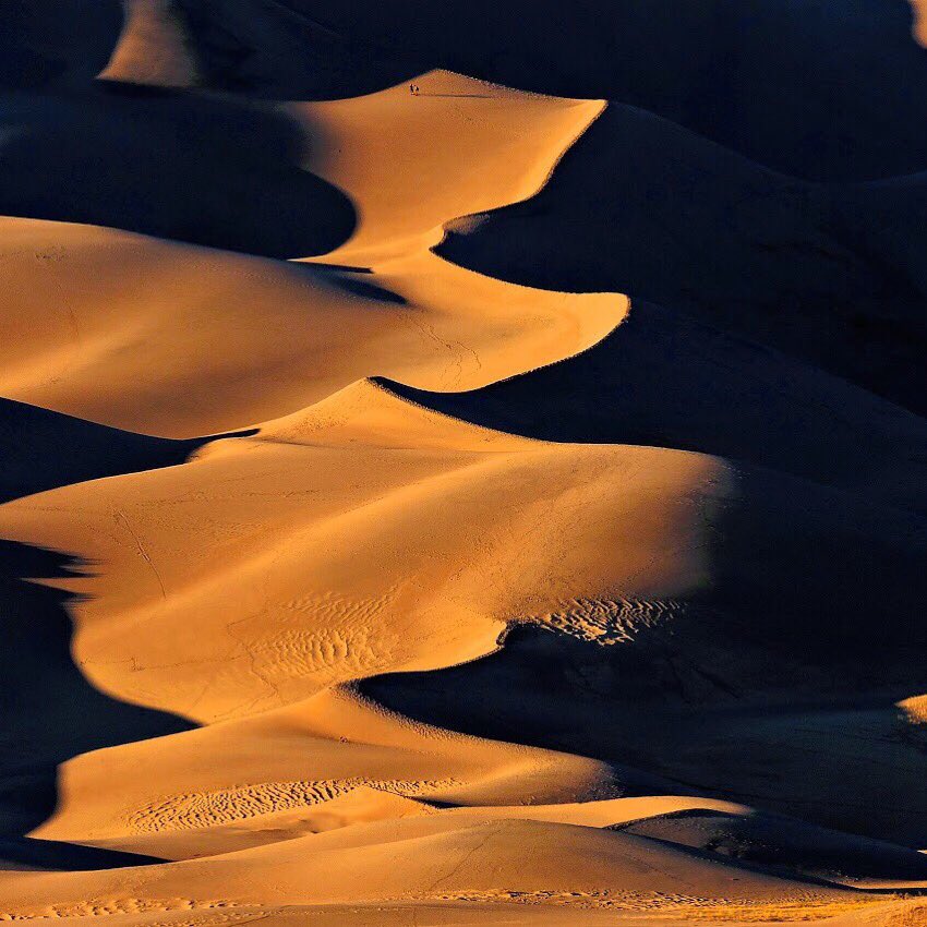 Two people stand like little dots on the side of a gigantic sand dune.