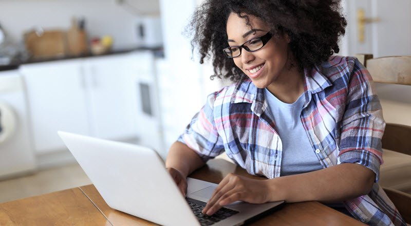 a smiling Black woman with glasses sitting at her desk looking at her taptop