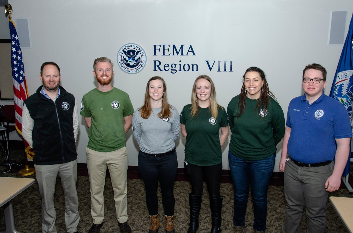 a group of 6 people standing in front of a sign that reads "FEMA Region VIII." From left to right, two men, followed by three women and one man. From left to right, the shirt colors are black, light green, grey, dark green, dark green, blue. The five on the left have a shirt with an AmeriCorps logo. The man on the left has a shirt with a FEMA logo on it.