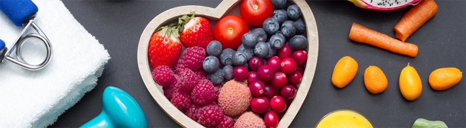 a photograph of berries in a heart shapeed bowl with various vegetables surrounding it.