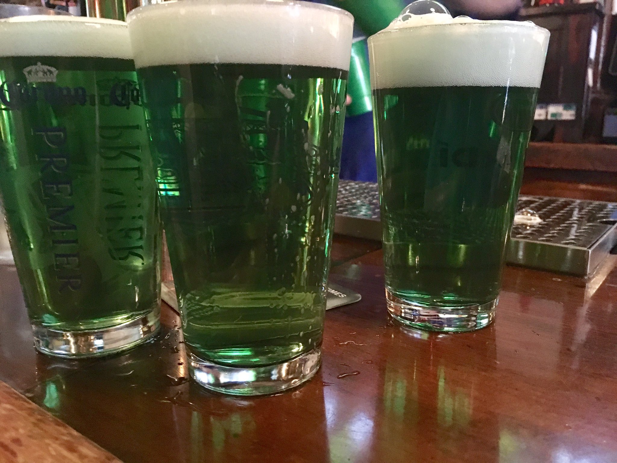 Three green beers on a bar.