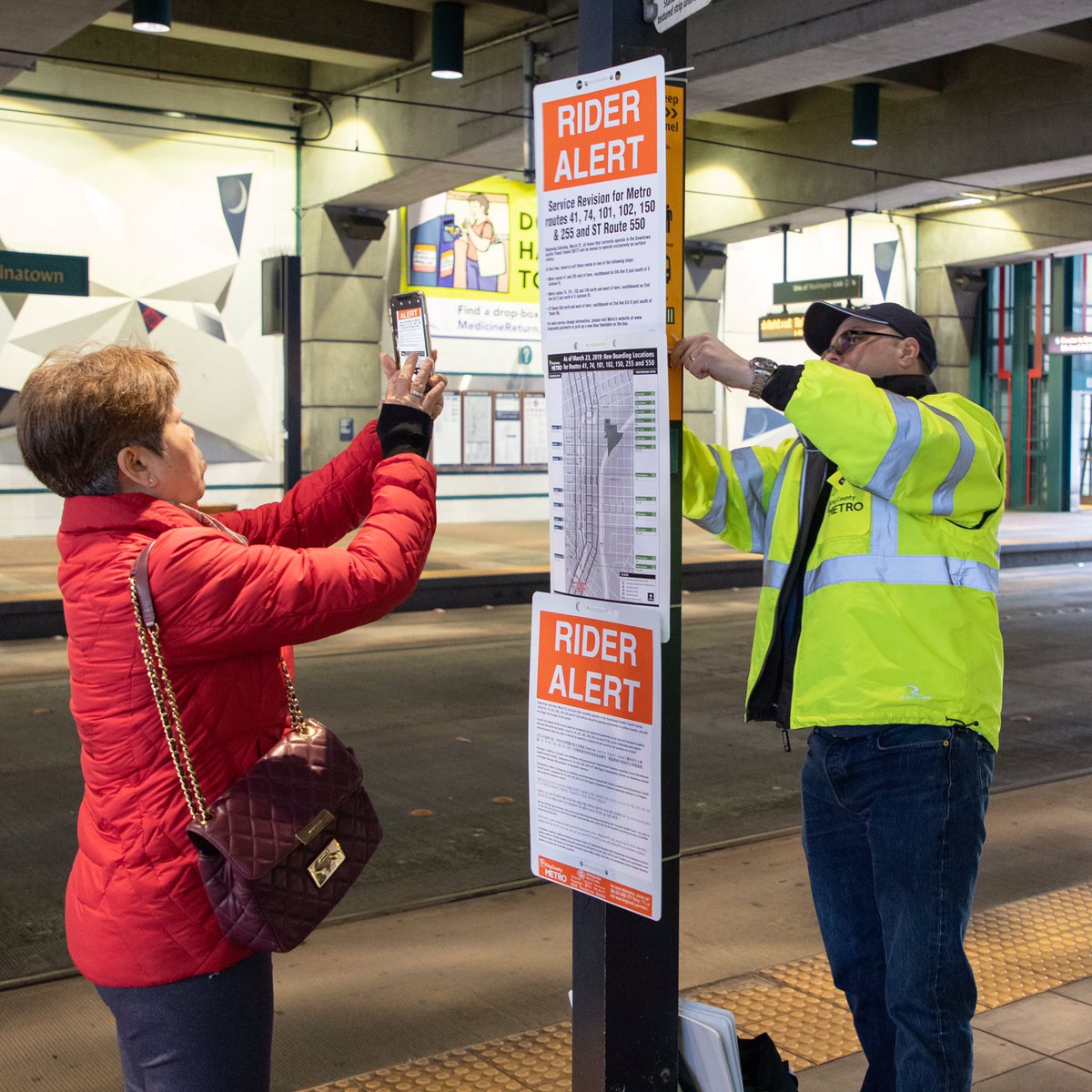 Metro staff installing rider alerts in the bus tunnel in February alerting riders to upcoming changes. A rider photographs the multi language notice.