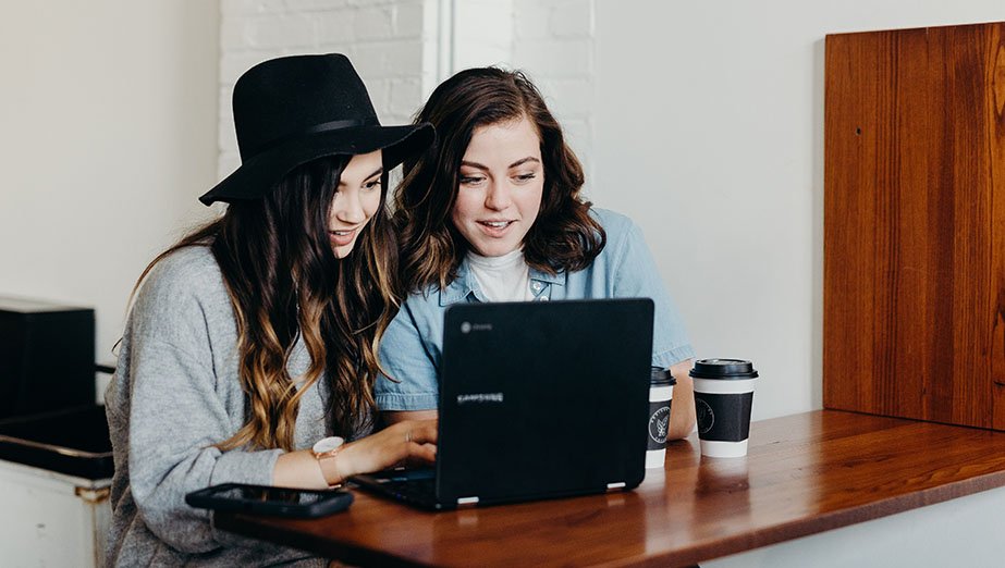 two young woman sitting siide by side on a laptop reading the screen and smiling