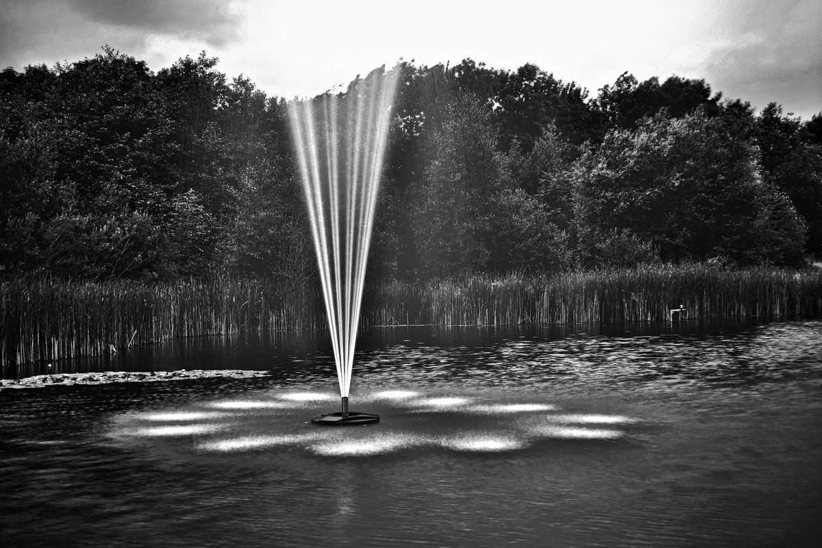 A monochrome photograph using a neutral density filter of the water fountain on the lake at the University of Nottingham's Jubilee Campus.