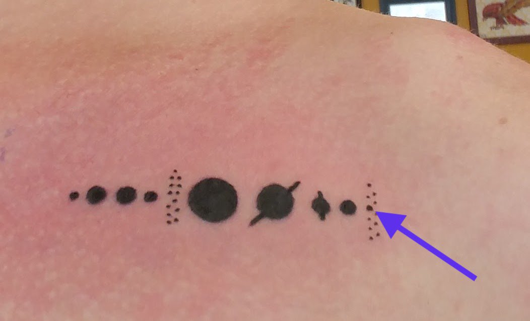 Image is my tattoo of the Solar System including planets, asteroid belt, and Kuiper belt. I overlaid an arrow pointing at Pluto for this post.