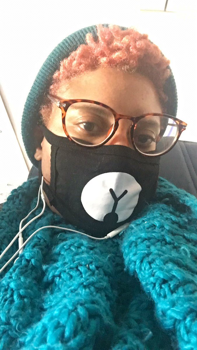 Tiffany wears a cute black and white bear face mask, blue scarf and hat while rocking peach colored hair and tortoise shell glasses. Her white earphones are also pictured.