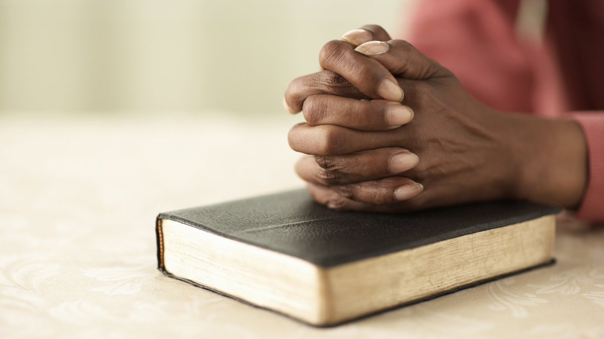 hands clasped over a book of scripture