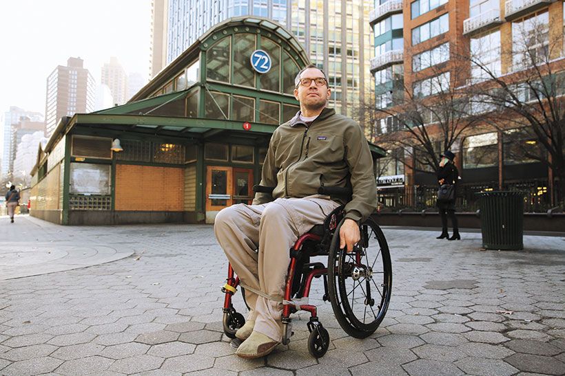 A profile photo of Sasha Blair-Goldensohn ’98 in his wheelchair, sitting outside a subway station. 