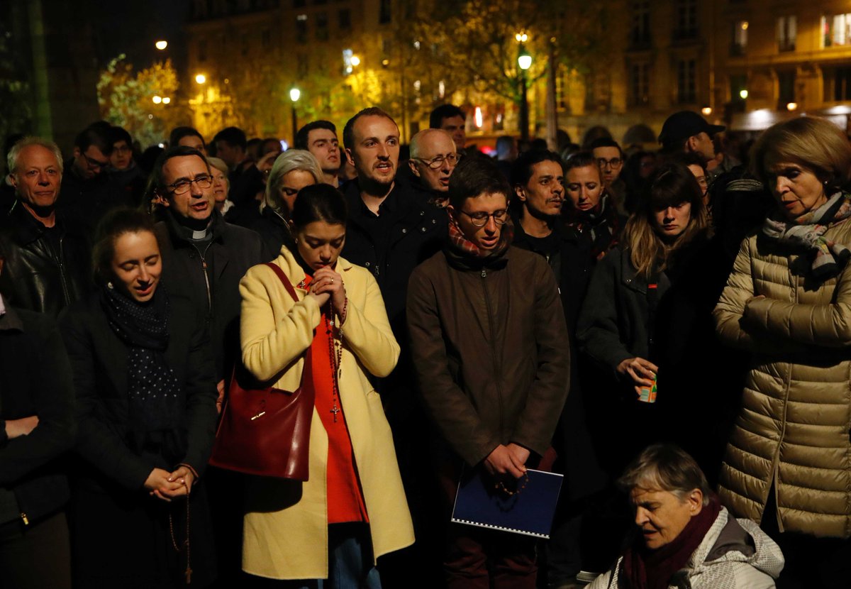 RaiNews's tweet photo. In ginocchio davanti a #NotreDame in fiamme: in migliaia a #Parigi pregano e cantano l'Ave Maria → https://t.co/QtuD7oXDnh https://t.co/38TGLsrsVZ