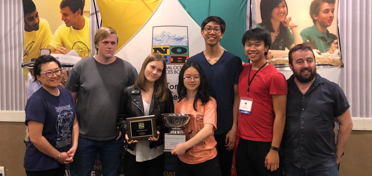 Albany High School students smile with a trophy and a plaque commemorating their National Ocean Science Bowl win. Their coach stands beside them.