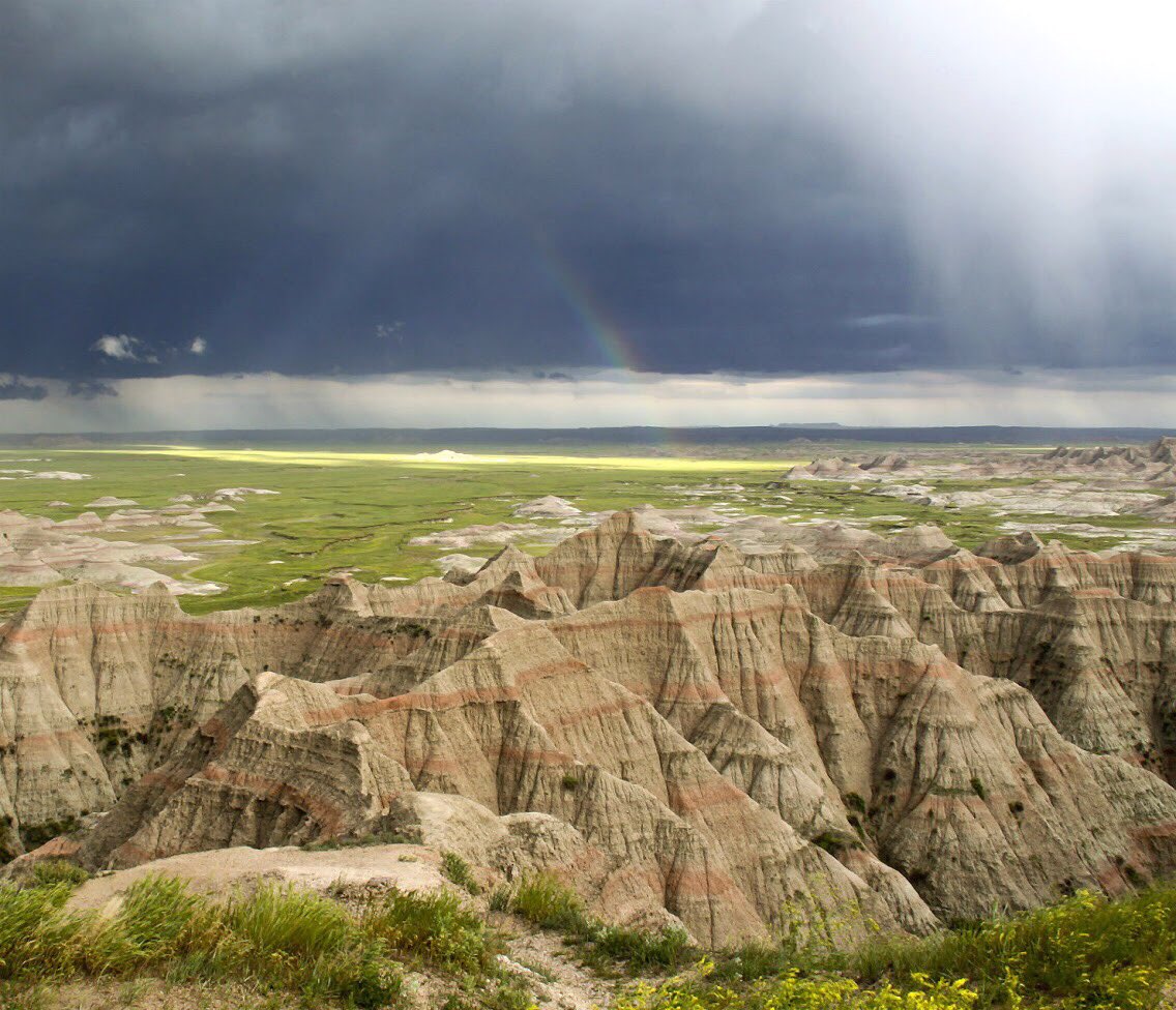 Storm clouds float over a landscape of rocky hills and flat grassy fields.
