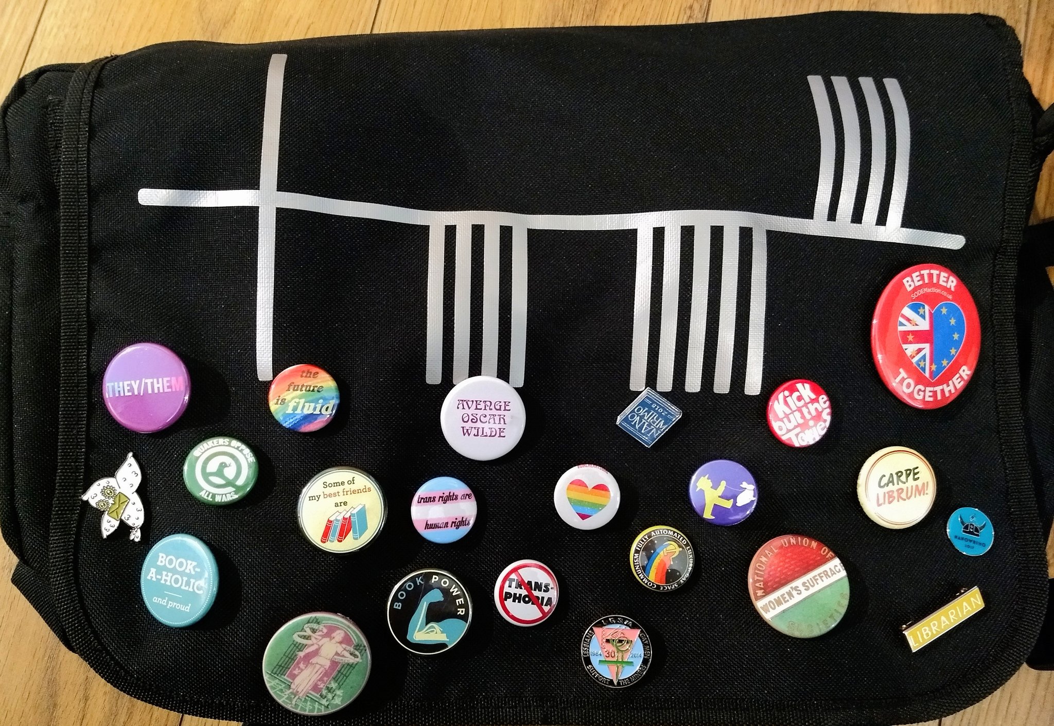 A black satchel covered in pin badges. Slogans include "trans rights are human rights", "avenge Oscar Wilde", "kick out the Tories" and "Quakers oppose all wars".
