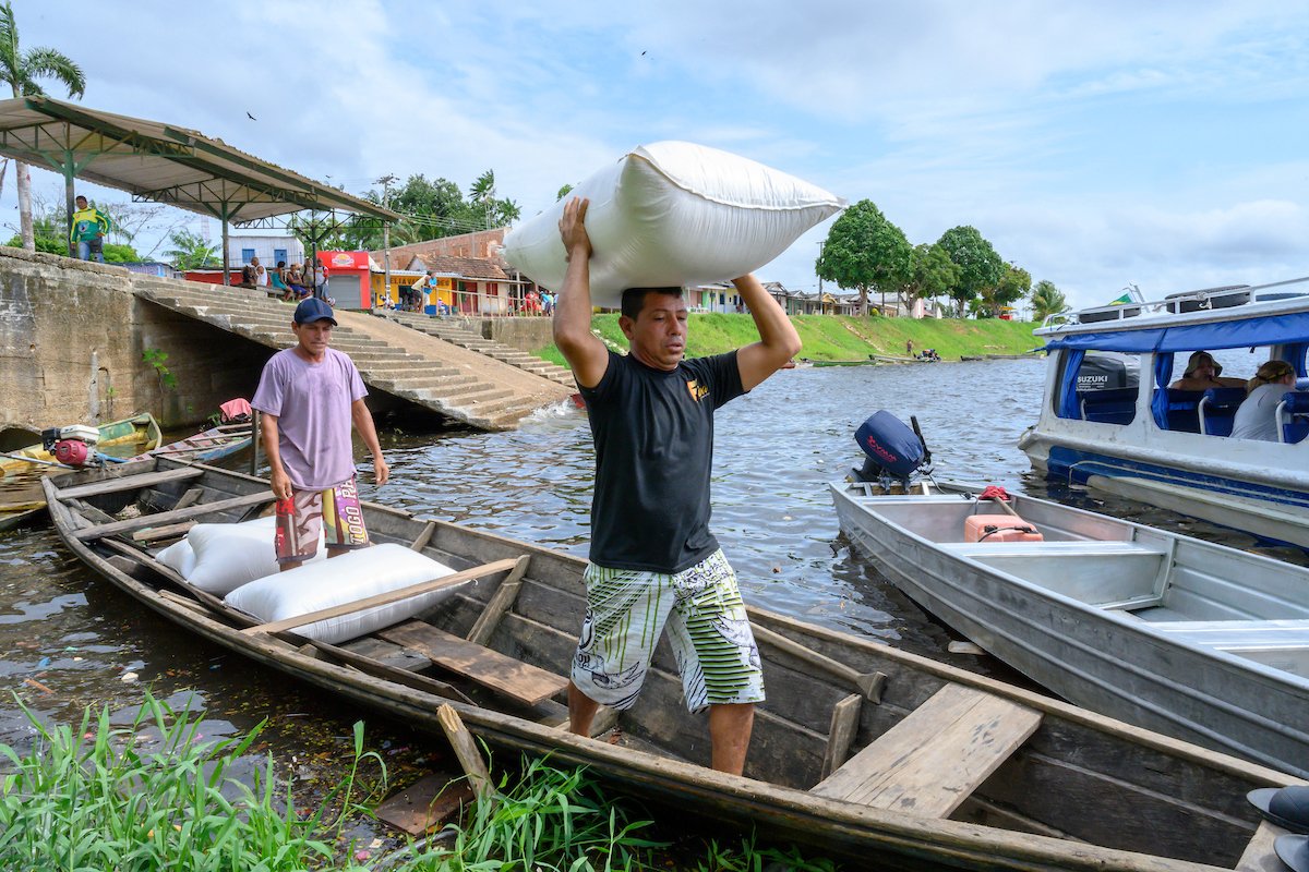 Men load large bags full of farinha onto a boat on a river in the Amazon rainforest