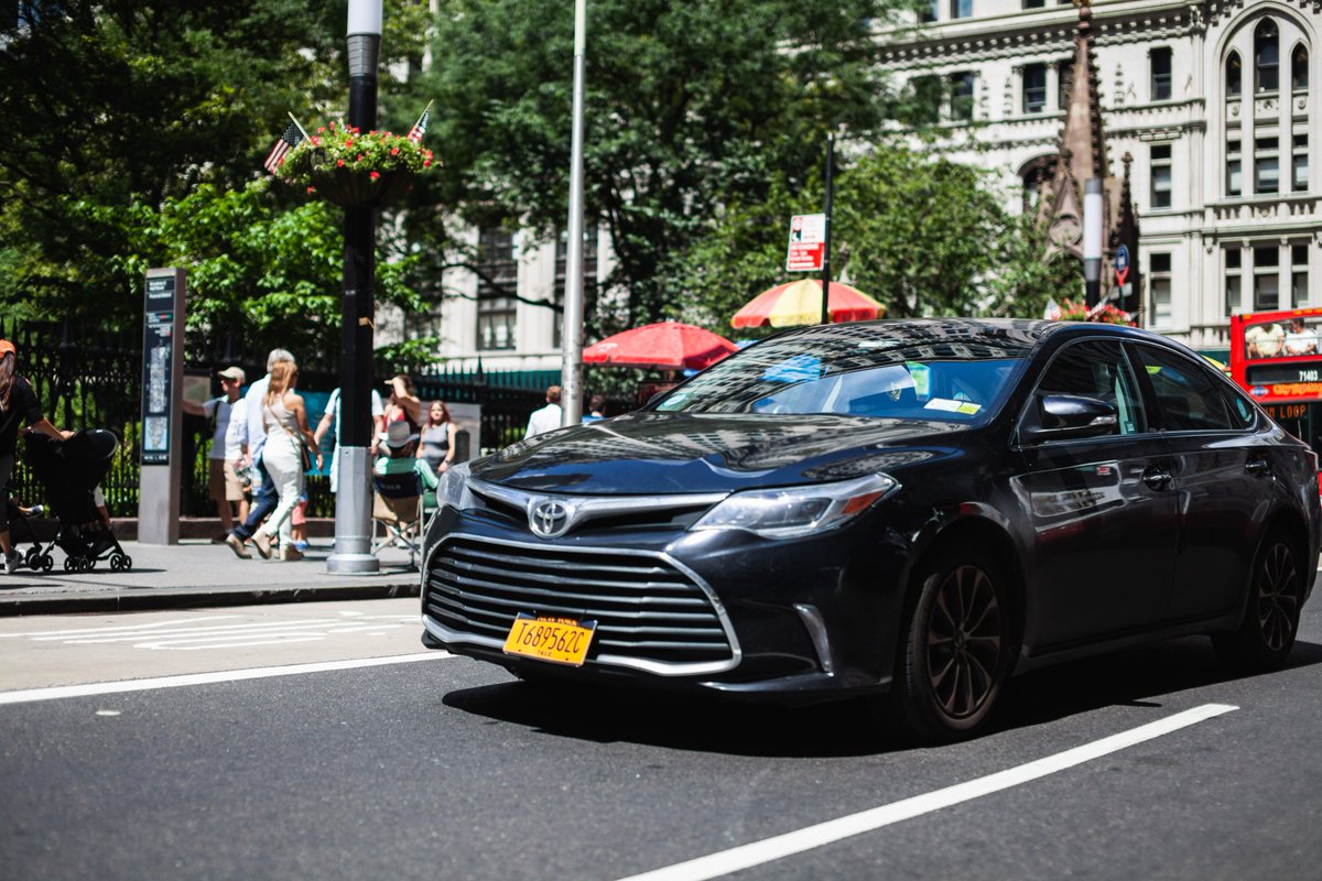 The image shows a black for-hire vehicle car on an NYC street.