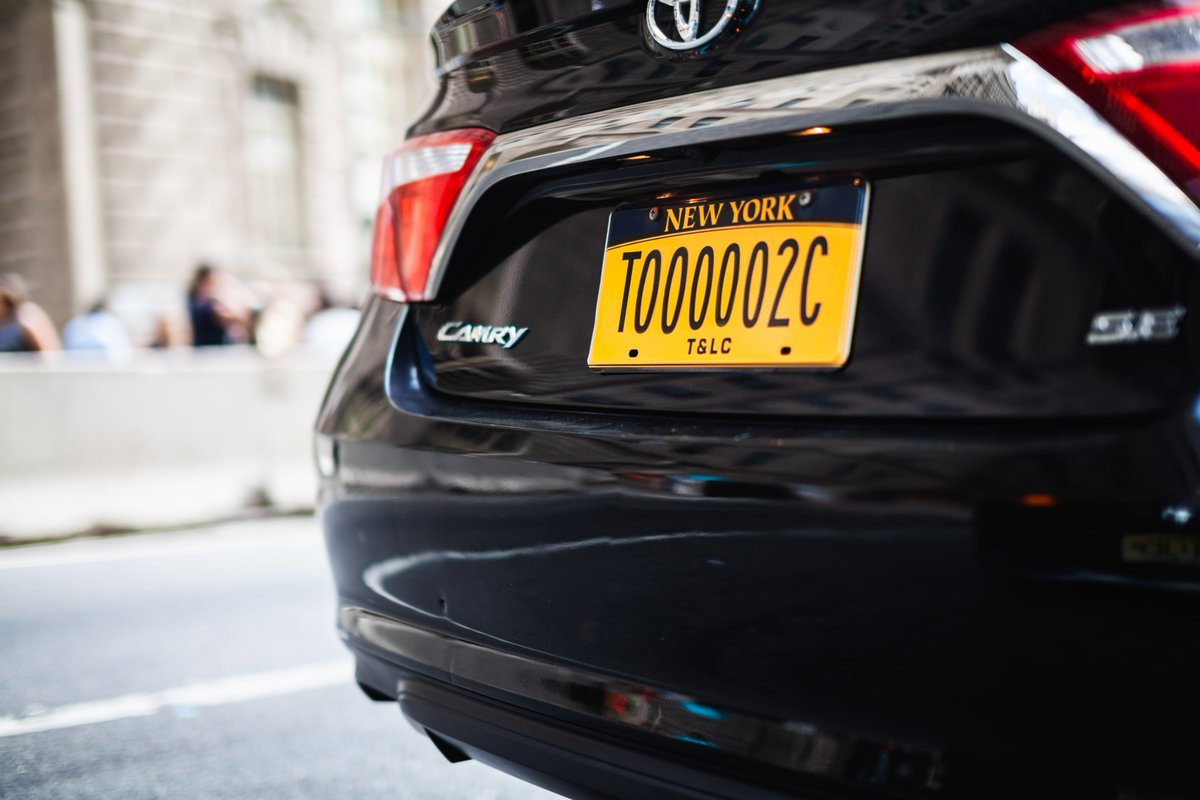 The image shows the license of a black for-hire vehicle car on an NYC street.