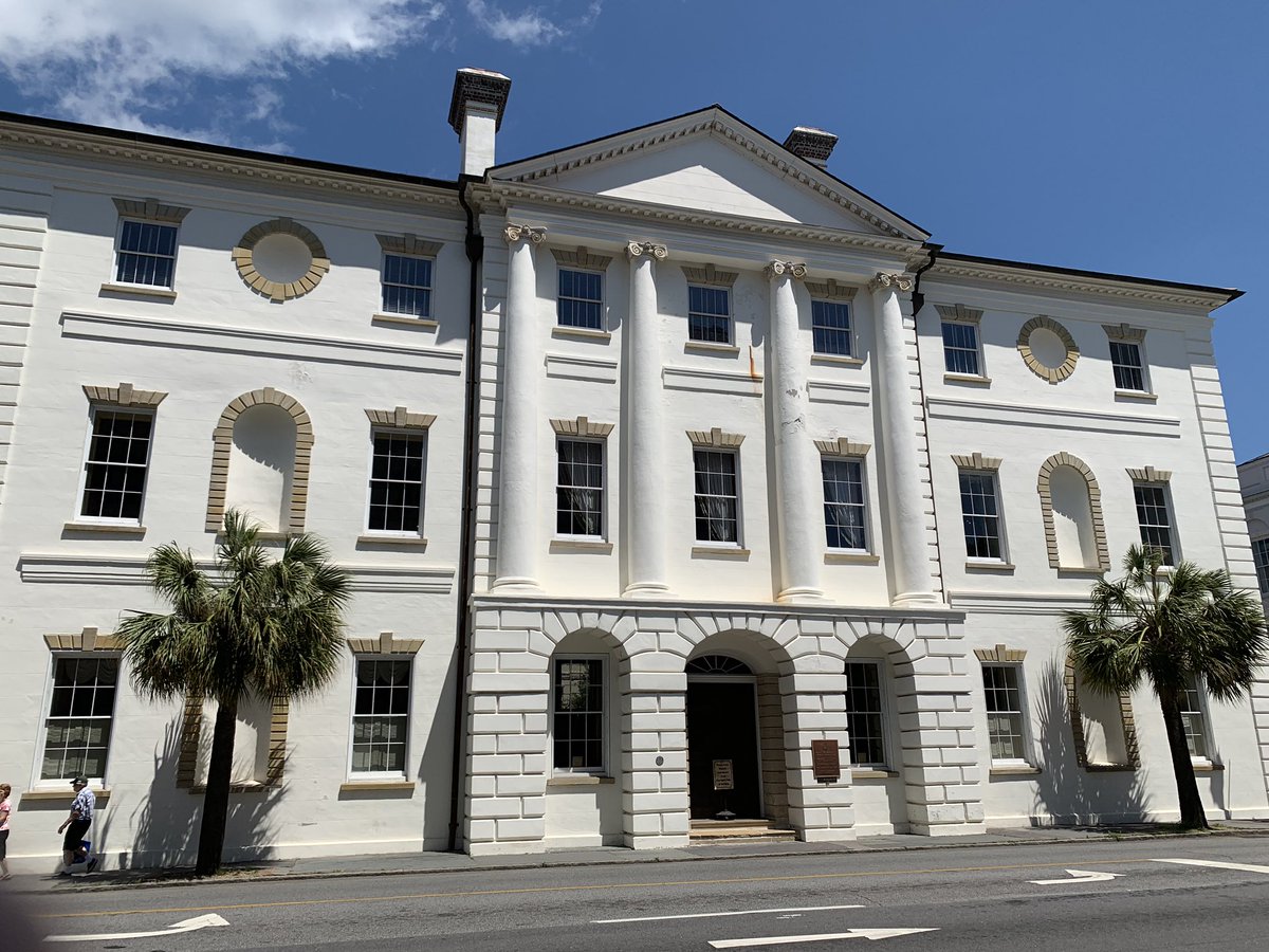 The Charleston County Courthouse. A white building with three stories, a Romanesque white stone facade, and two palm trees out front.