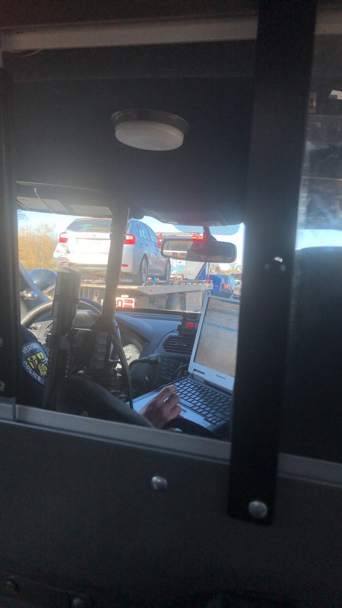 looking from the backseat of a police car at a damaged car on a tow truck