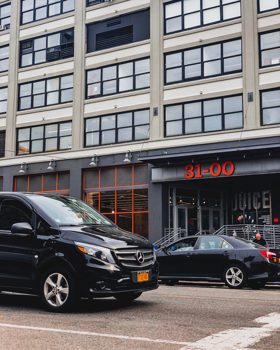 The image shows two black-colored cars on an NYC street, near a large office and retail building.