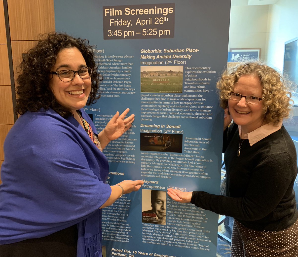 Photo to accompany bio of Chambers (who stands to the left) and Kalin (on the right). They are pointing to a large sign that lists the day's film screening, one of which is Dreaming in Somali.