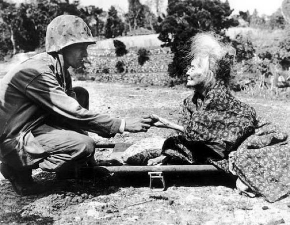 BarbaraPAuthor's tweet photo. #USMarine Fenwick H. Dunn gives a candy bar from his #KRation to an elderly #Okinawa resident, sitting on a stretcher. 1945. #WW2 #Humanity https://t.co/nG7UfsqI97