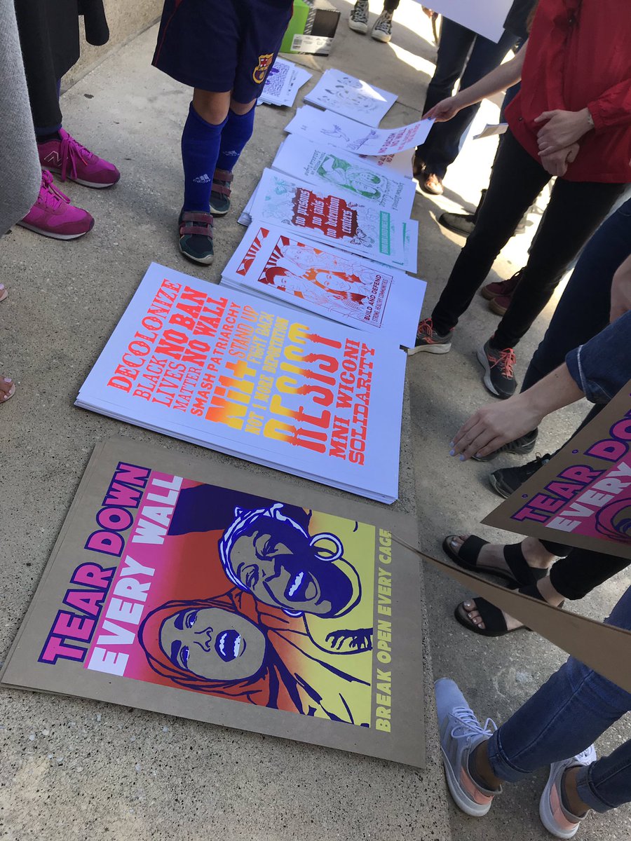 A group of colorful posters with liberators messages are in stacks with people gathered around.