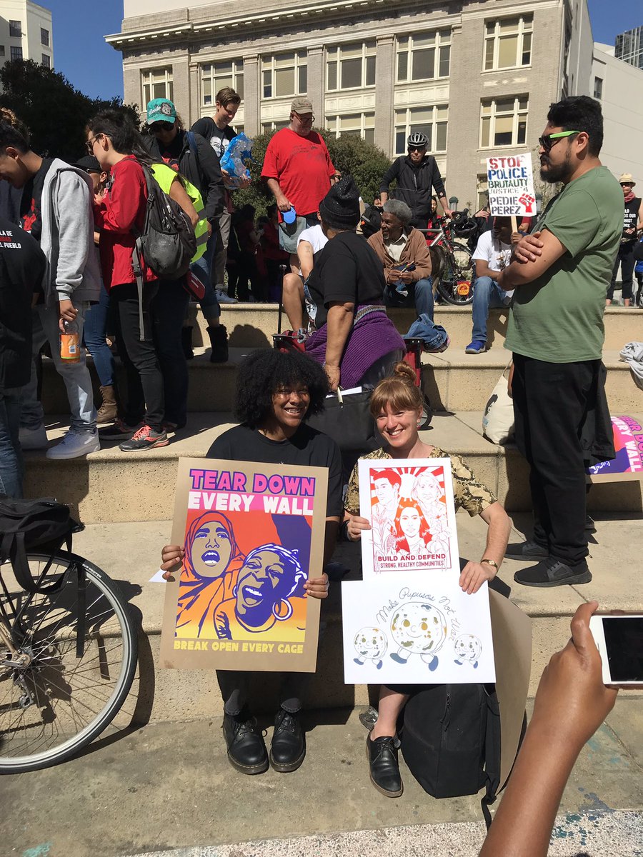 Two people hold up a few different posters among the crowd, smiling.