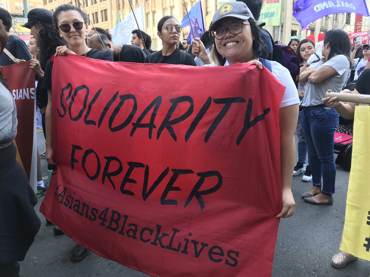 Two Asian people hold a banner that reads “Solidarity Forever #Asians4BlackLives”