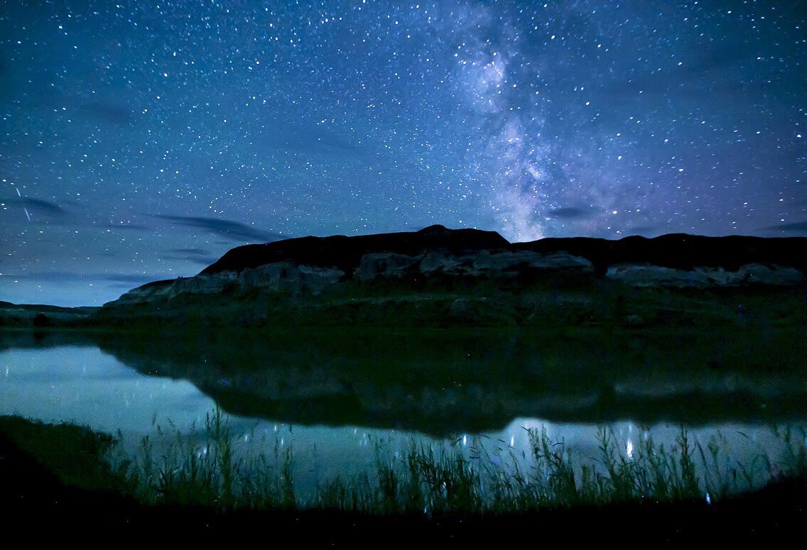 A wide calm river reflecting the starry night sky above.