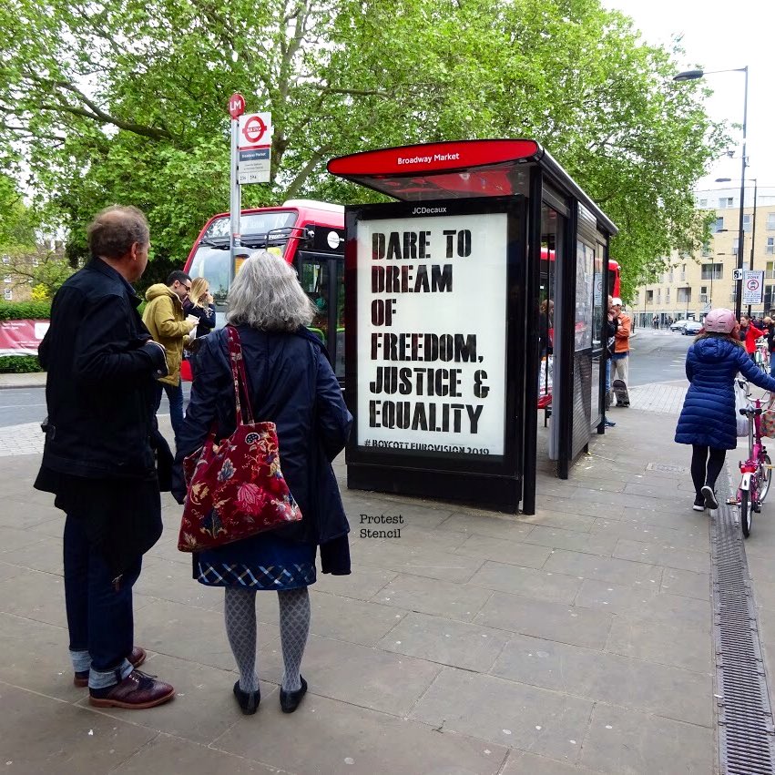 Man and woman look at bus stop poster reading ‘Dare to Dream of freedom, justice & equality’