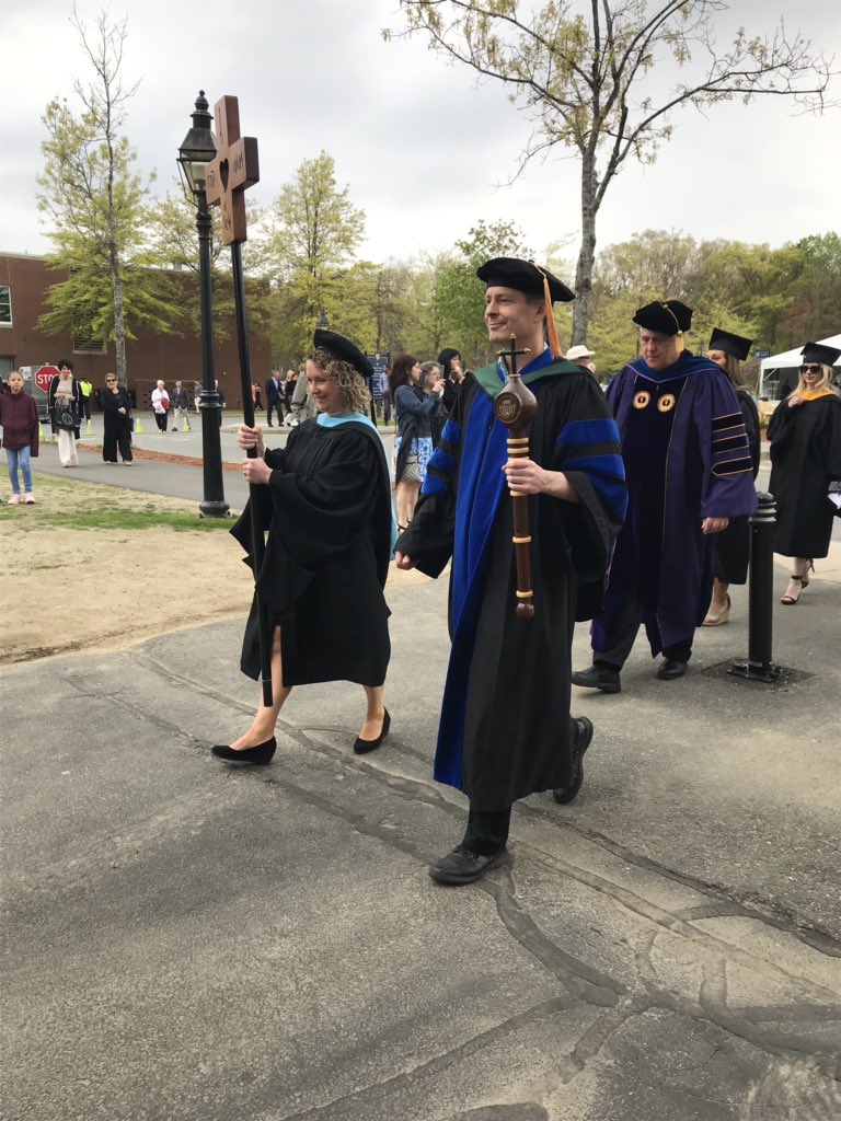 Merrimack's tweet photo. Leading the academic procession is Associate Professor Craig Looney, President of the Faculty Senate, carrying the University Mace. The mace was fashioned for the 1986 Commencement by Cistercian Monks of the Holy Rood Guild at Saint Joseph’s Abbey in Spencer, MA #MackGrad https://t.co/9evr3h6SC4