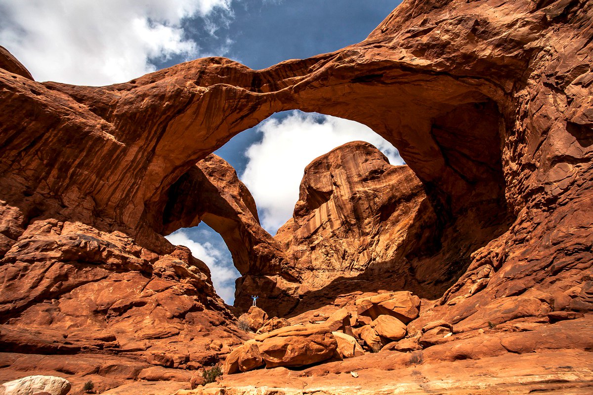 A massive sandstone arch has two large red rock spans curving between two cliffs.