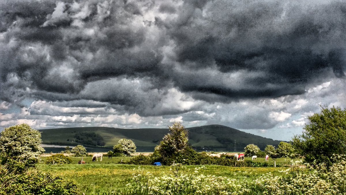 A dark hill on a bright day, under dramatic dark clouds