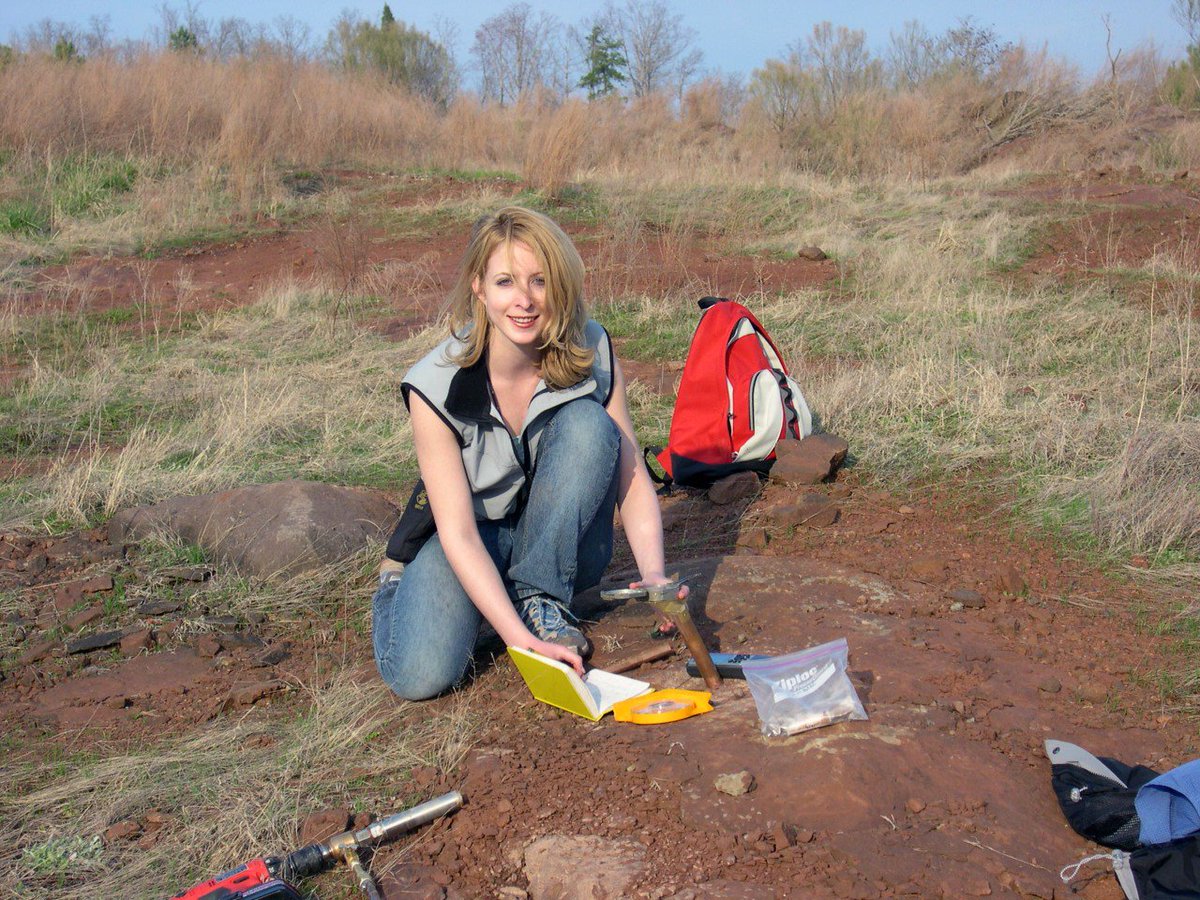 Dr. Jessica Whiteside in the field surrounded by grass and dirt. She is taking samples to study Earth's past magnetic reversals.